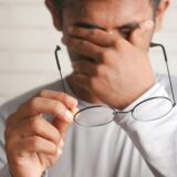 Man covering his eyes and holding a pair of glasses