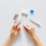 Contact lens on fingertip with contact lens cases on desk