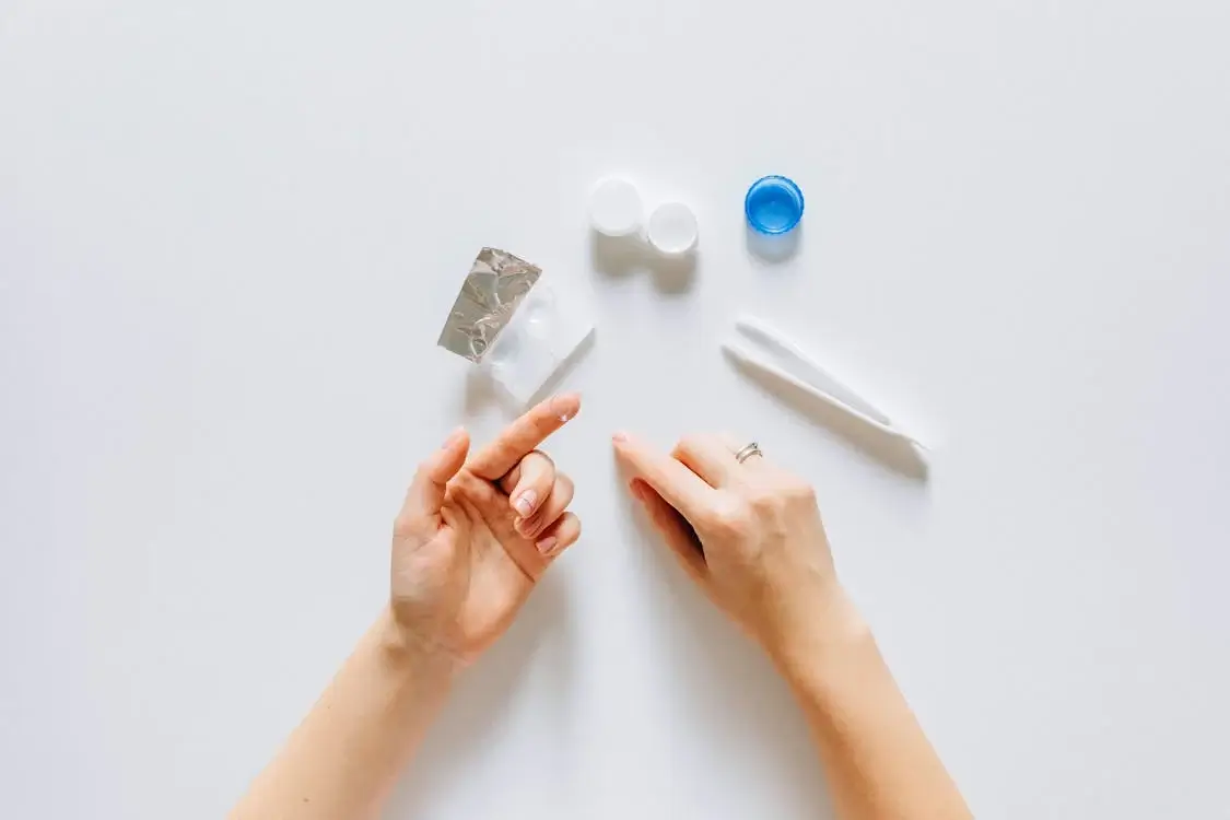 Contact lens on fingertip with contact lens cases on desk