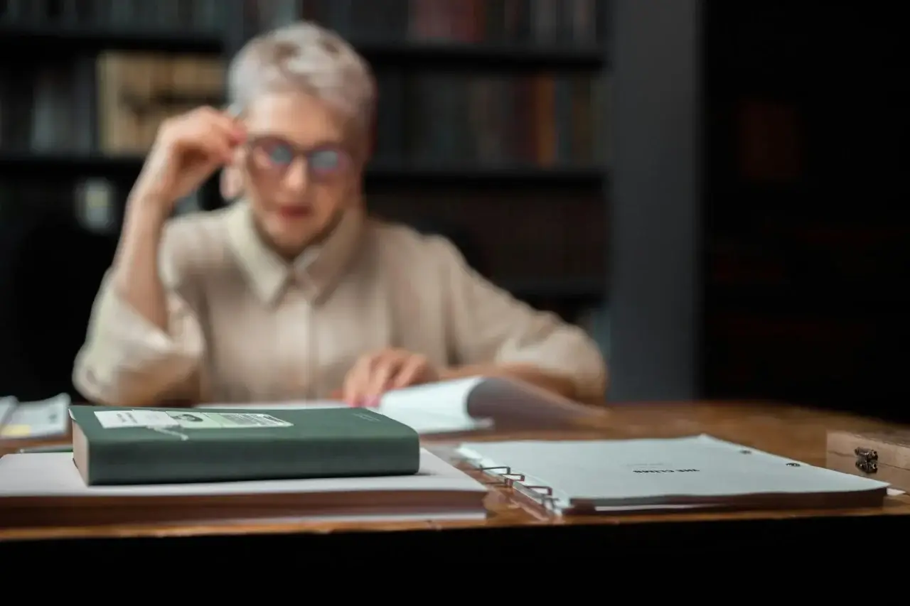 Desk with books and papers in front of woman in glasses